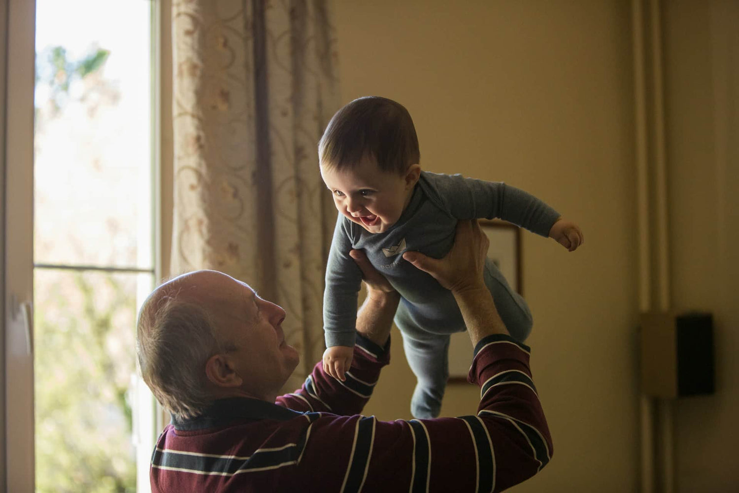 Hombre de la tercera edad sosteniendo a niño sonriente en el aire